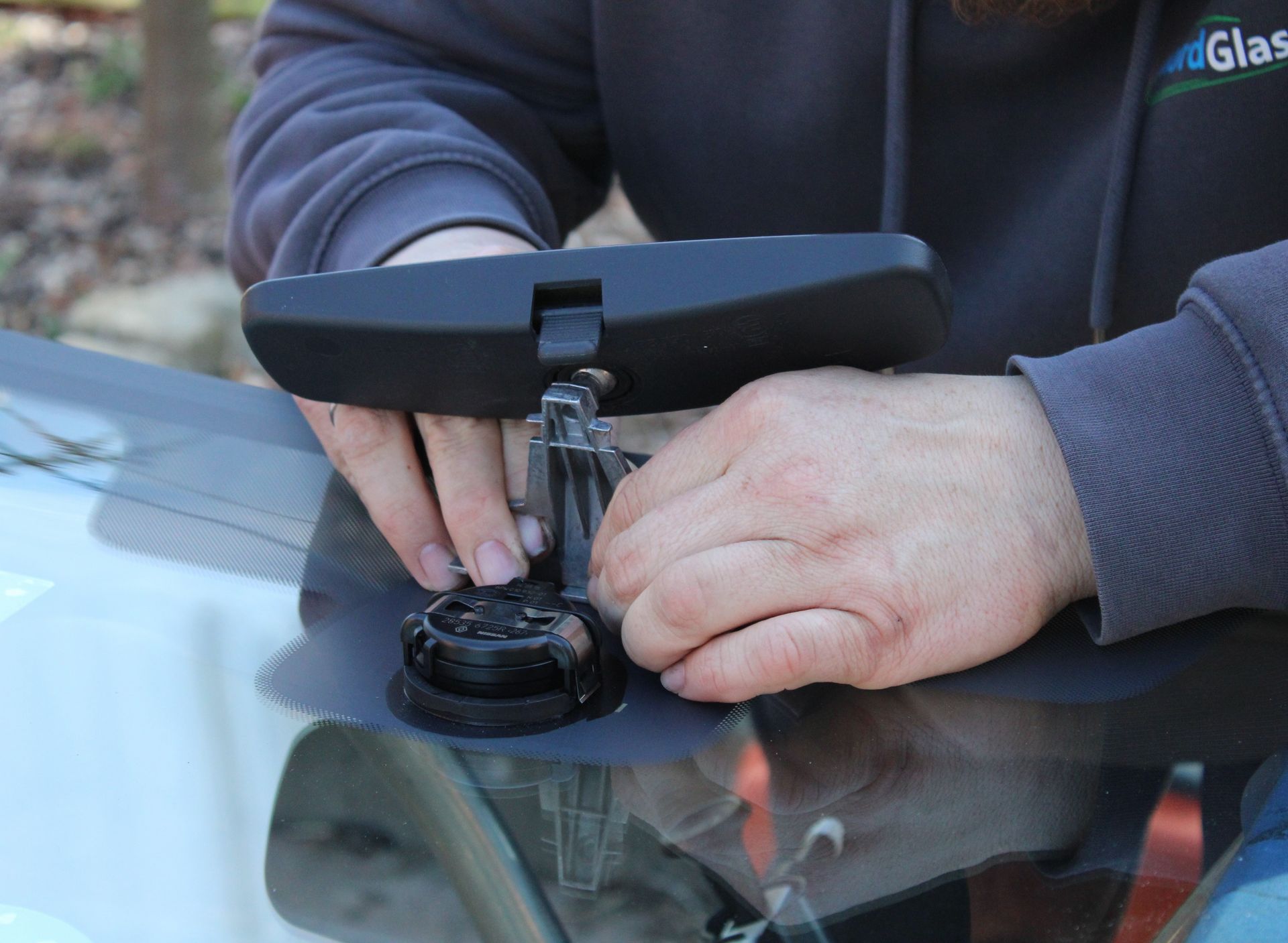 Wiederanbringen des Rückfahrtspiegel an der neuen Windschutzscheibe eines Fahrzeugs.